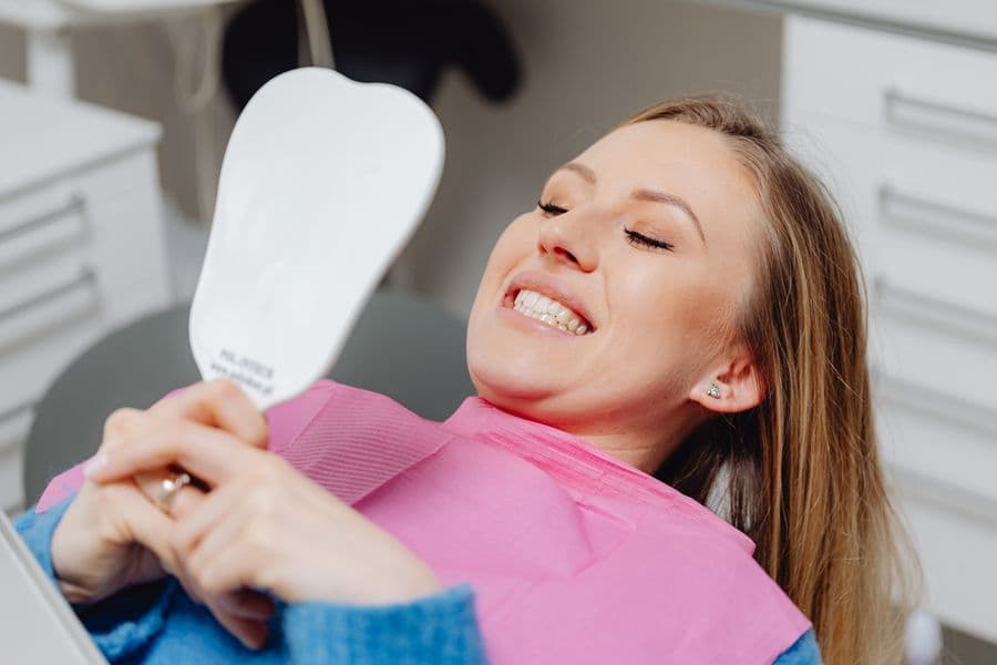 A happy patient checking their smile in a mirror at the dentist